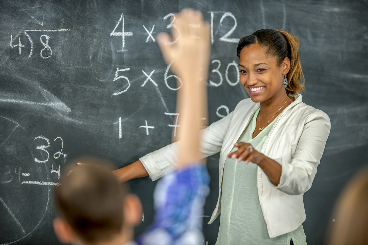 teacher at chalkboard pointing at student with hand raised teacher at chalkboard pointing at student with hand raised