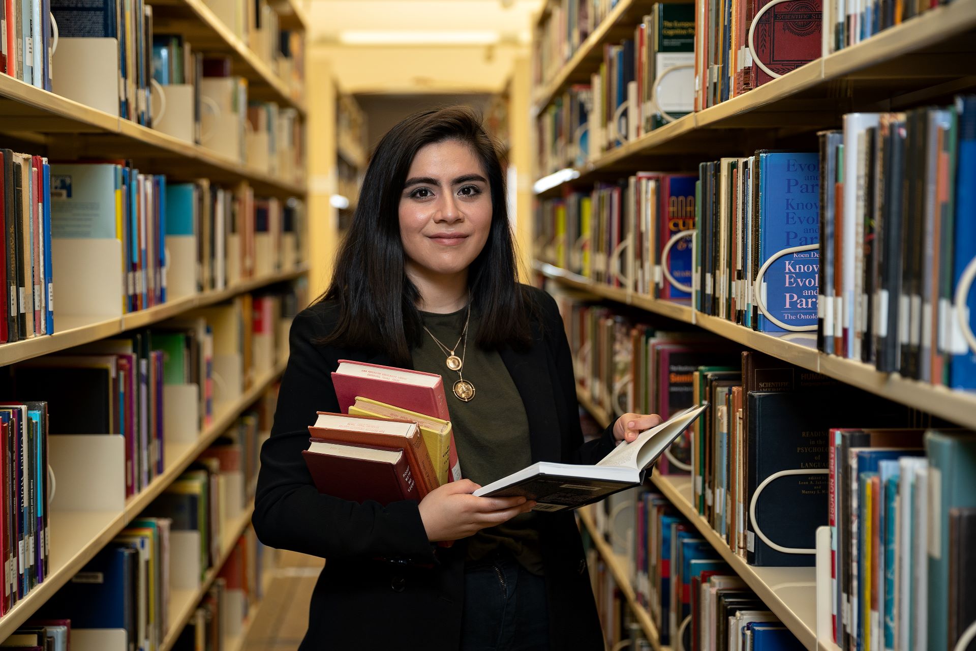Female student in library aisle with book in hand Female student in library aisle with book in hand