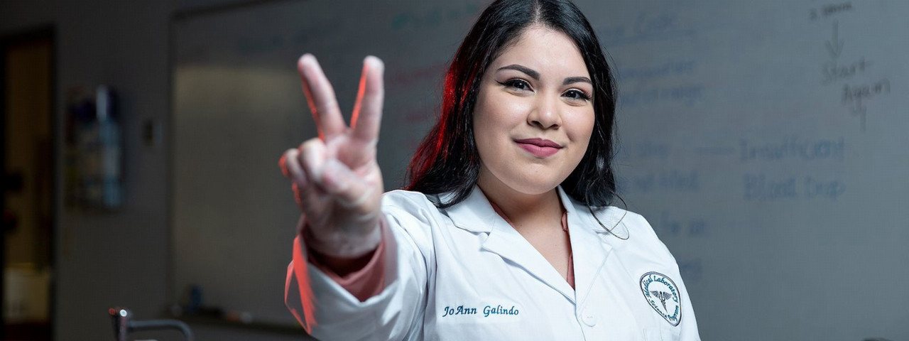Student wearing lab coat signals v's up