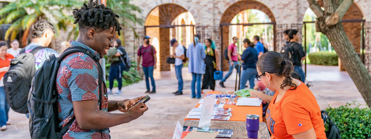 Students walking outside UTRGV campus with student stopping at a table set up by school organization.